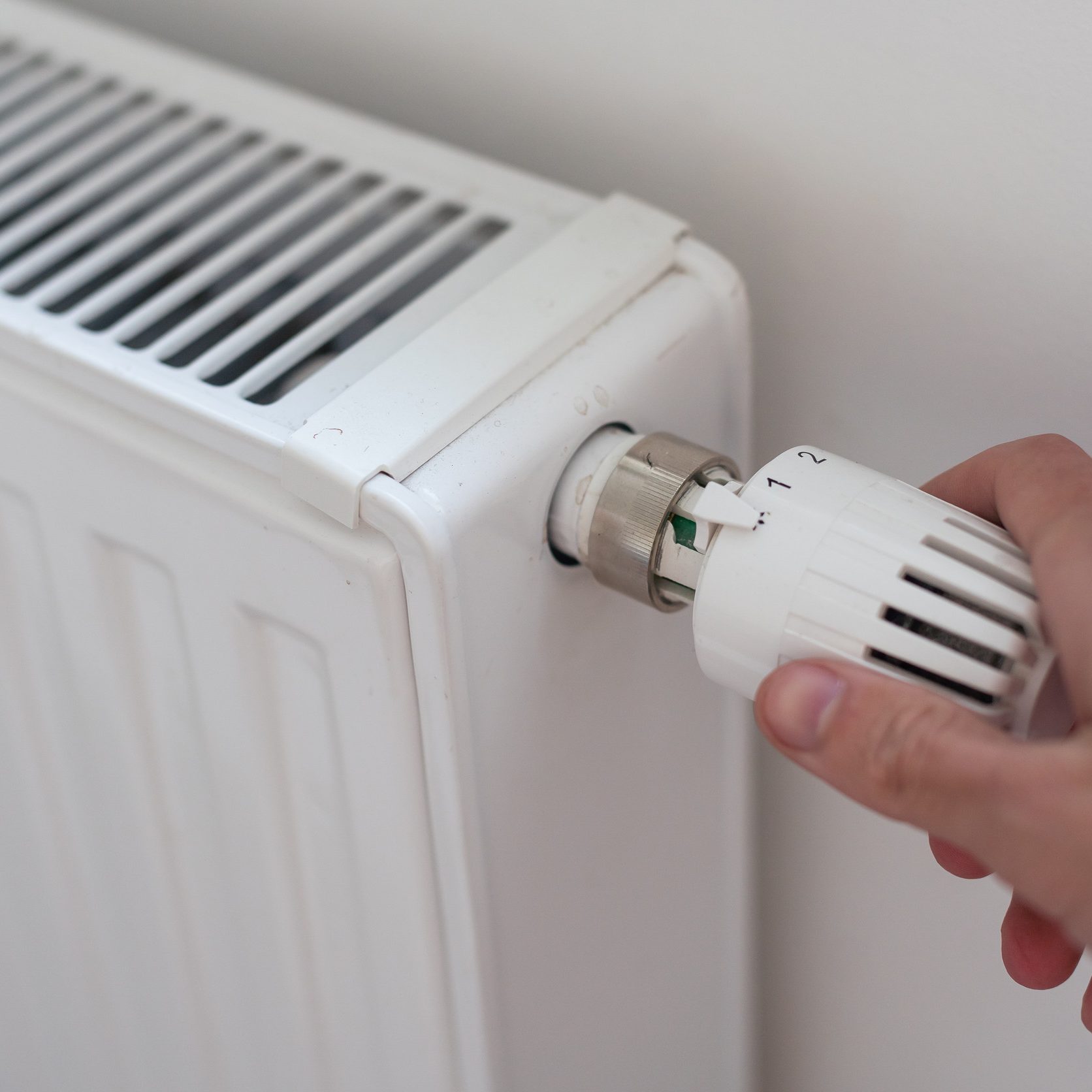 Hand adjusting thermostat valve of heating radiator in a room. High quality photo