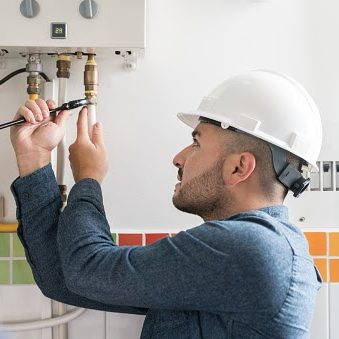 Portrait of a Latin American Repairman installing a natural gas boiler at a house using a wrench - home improvement concepts
